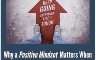 A digital graphic featuring a first-person perspective of someone’s feet standing on a road with a red arrow pointing forward, displaying the text “KEEP GOING EVEN WHEN LIFE IS TOUGH.” The surrounding frame includes the title “Why a Positive Mindset Matters When Motivations Change” and a JMS logo in the top right corner.